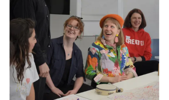 Group of 4 adults sitting at a table and 1 standing, all talking at Arts Society event
