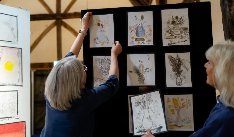 Two Arts Society volunteers hang pictures on a wall