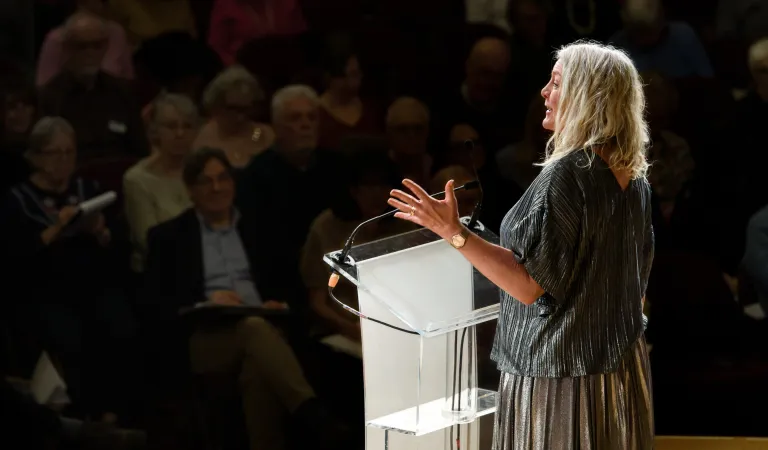 A woman addresses a large audience from behind a podium 